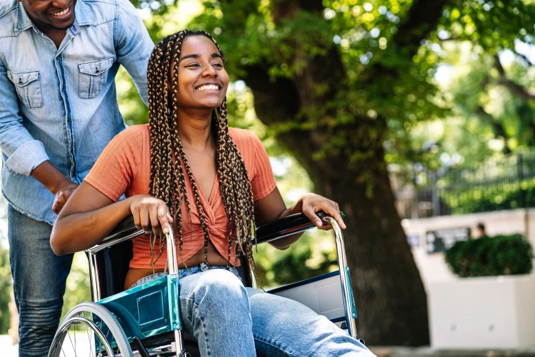 Woman in wheelchair smiling with support worker behind her